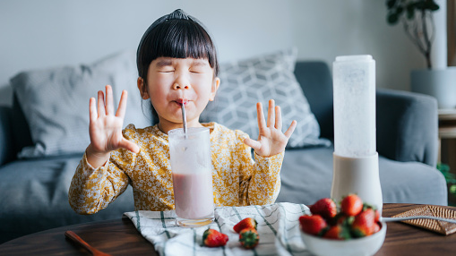 young girl making a sour face while sipping a strawberry smoothie